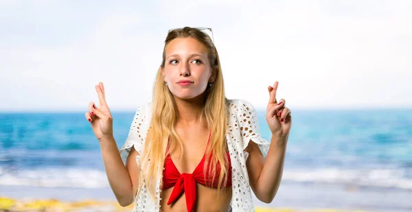 Blonde girl in summer vacation with fingers crossing and wishing