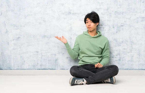 Asiatischer Mann Sitzt Auf Dem Boden Und Macht Zweifel Geste — Stockfoto