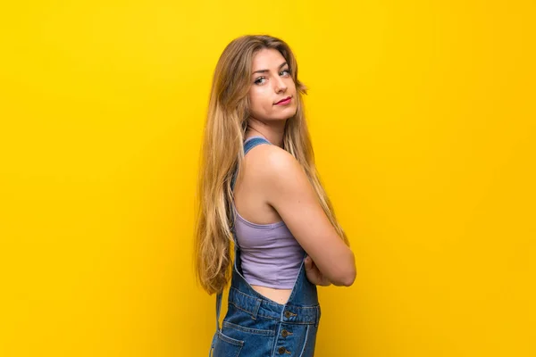 Jovem Loira Com Macacão Sobre Fundo Amarelo Isolado Rindo — Fotografia de Stock