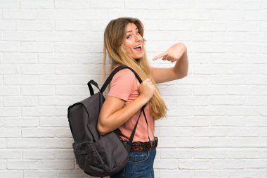 Sırt çantalı, beyaz tuğlalı duvarın üzerinden geçen genç sarışın kadın.