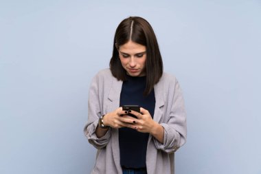 Young woman over isolated blue wall sending a message with the mobile
