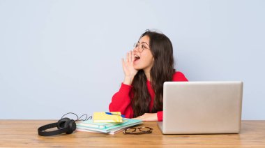 Genç öğrenci kız lateral ağız geniş açık bağırarak bir masada okuyan