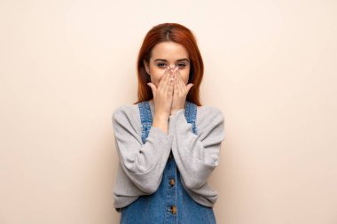 Genç kızıl saçlı kadın, izole edilmiş arka planda gülümserken ağzını kapatıyor.