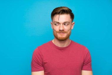 Izole mavi duvar ayakta redhead adam ve yan bakıyor