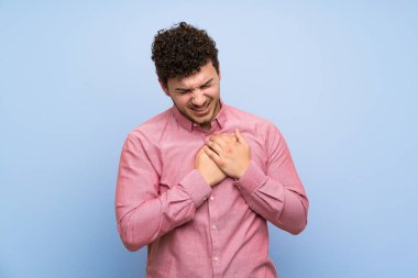 Izole mavi duvar üzerinde kıvırcık saçlı adam kalbinde bir ağrı olan