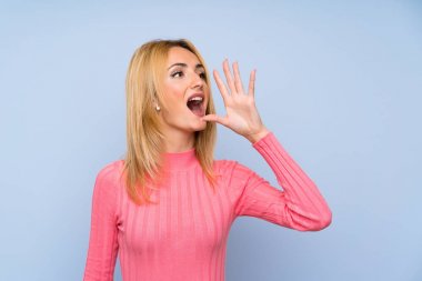 Soyutlanmış mavi arka planda pembe kazaklı genç sarışın kadın ağzı açık bağırıyor.