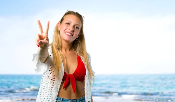 Chica rubia en vacaciones de verano sonriendo y mostrando signo de victoria — Foto de Stock