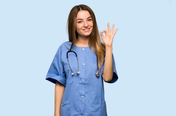 Jonge Verpleegster Toont Een Teken Met Vingers Geïsoleerde Blauwe Achtergrond — Stockfoto