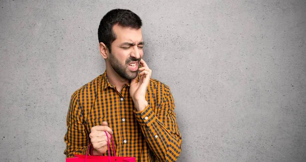 Man with shopping bags with toothache over textured wall