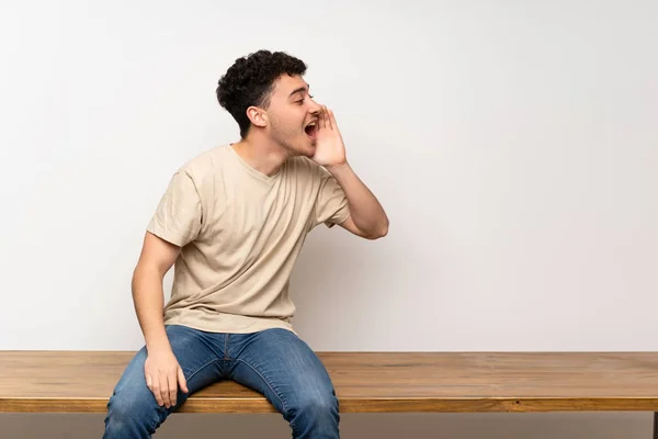 Jovem Sentado Mesa Gritando Com Boca Bem Aberta Para Lateral — Fotografia de Stock