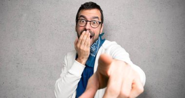 Gözlüklü yakışıklı adam birini parmağıyla işaret ediyor ve dokulu duvara gülüyor