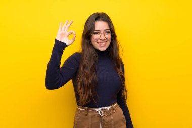Parmakları ile ok işareti gösteren izole sarı duvar üzerinde Genç kız