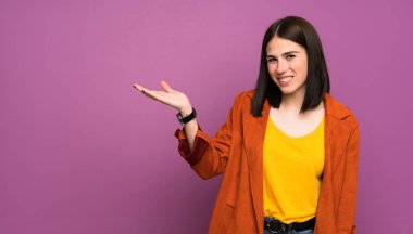 İzole edilmiş mor arka planda ceketi olan genç bir kadın avucunun içinde hayali bir mekan tutuyor.