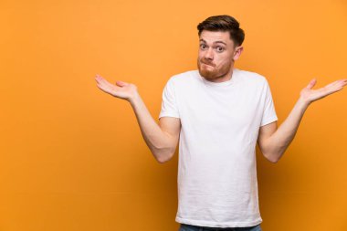 Kırmızı saçlı adam kahverengi duvar üzerinde elleri kaldırırken şüpheleri olan