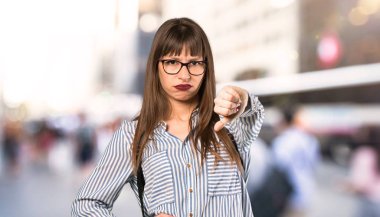 Açık havada negatif ifade ile başparmak aşağı gösteren gözlük ile kadın