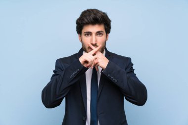 İzole mavi duvar üzerinde sessizlik jesti bir işaret gösteren işadamı