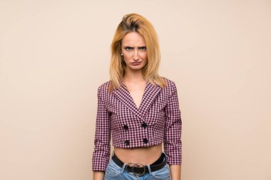 Pembe ceketli genç sarışın kadın üzgün ve depresif bir ifadeyle tecrit edilmiş duvarın üzerinde.