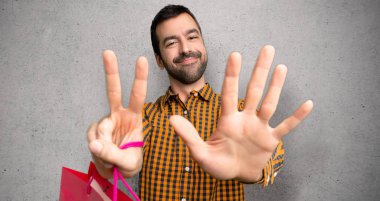 Dokulu duvar üzerinde parmakları ile yedi sayma alışveriş çantaları ile Adam