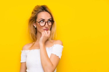 Gözlüklü izole sarı duvar üzerinde genç sarışın kadın