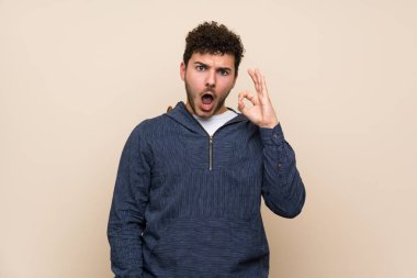 İzole duvar üzerinde kıvırcık saçlı Adam şaşırttı ve ok işareti gösteren