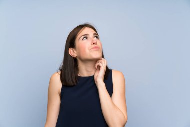 Izole mavi duvar ayakta ve bir fikir düşünme üzerinde genç kadın