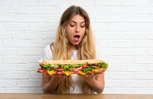 Wanita Pirang Muda Yang Memegang Sandwich Besar Membuat Gerakan Kejutan — Stok Foto