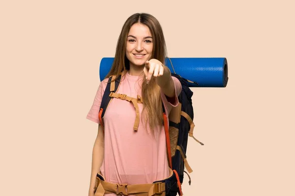 Young backpacker woman points finger at you with a confident expression on isolated yellow background