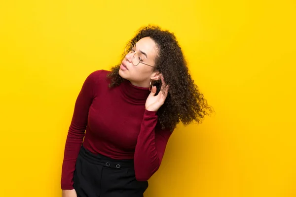 Dominican woman with turtleneck sweater listening to something by putting hand on the ear