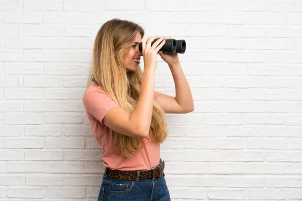 Mujer Rubia Joven Sobre Pared Ladrillo Blanco Con Prismáticos Negros —  Fotos de Stock