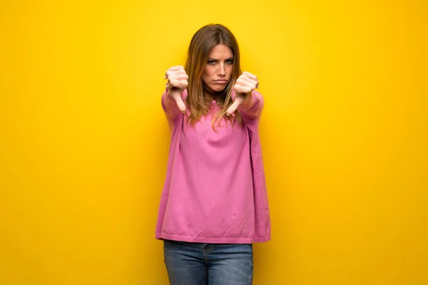女性とともにピンクセーター以上黄色の壁ショー親指ダウン — ストック写真