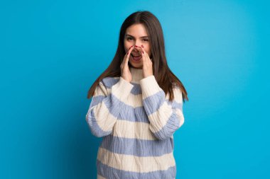 Mavi duvarın arkasında genç bir kadın bağırıyor ve bir şeyler söylüyor.