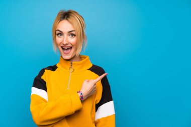 İzole edilmiş mavi arka planda genç sarışın bir kadın var.