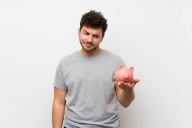 Büyük bir kumbara tutan izole duvar üzerinde kıvırcık saçlı adam