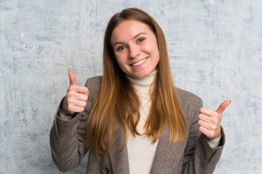 Homurdanan duvarın üzerinde genç bir kadın baş parmak hareketi yapıyor.