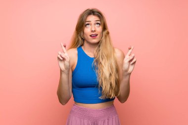 Soyutlanmış pembe arka planı olan genç sarışın kadın, şans diliyor ve en iyisini diliyor.