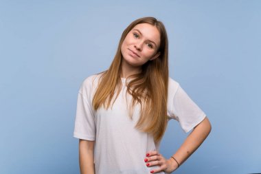 Mavi duvarın arkasında genç bir kadın kolları kalçasında ve gülümsüyor.