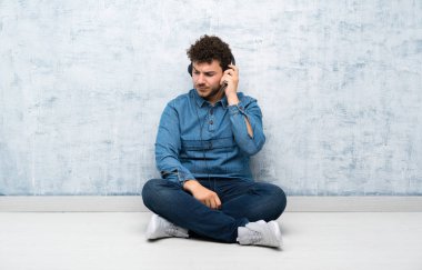 Yerde oturan genç adam kulaklıkla müzik dinliyor