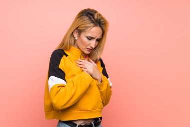 Soyutlanmış pembe arka planı olan genç sarışın bir kadın. Kalbinde ağrı var.