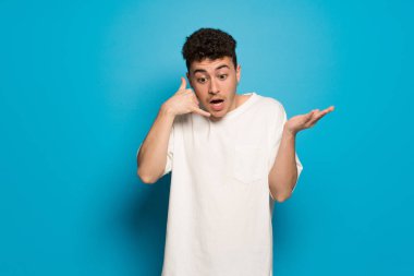 Mavi arka plandaki genç adam şaşırdı ve telefon hareketinde bulundu.