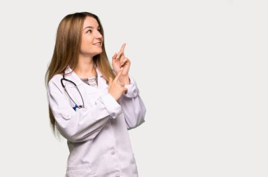 Young doctor woman pointing with the index finger and looking up on isolated grey background