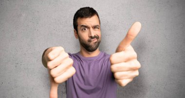 Yakışıklı adam iyi-kötü işareti yapıyor. Evet ya da dokulu duvar üzerinde kararsız