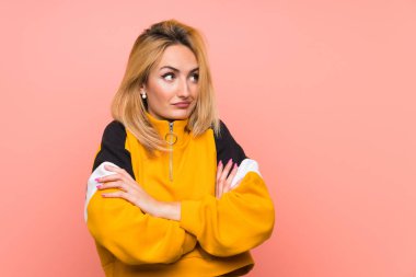 Soyutlanmış pembe arka planı olan genç sarışın kadın omuzlarını kaldırırken şüphe jestleri yapıyor.