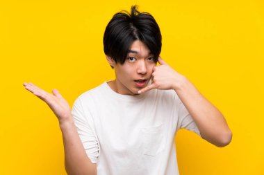Izole sarı duvar üzerinde Asyalı adam telefon jest yapma ve şüphe