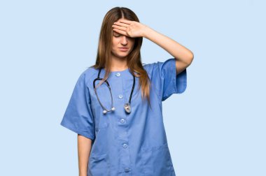 İzole edilmiş mavi arka planda yorgun ve hasta suratlı genç hemşire.