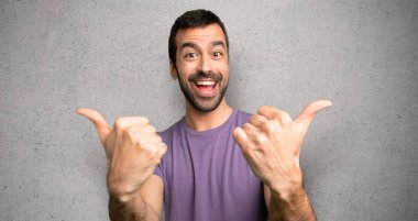 Yakışıklı adam iki eliyle jest kadar bir başparmak veren ve dokulu duvar üzerinde gülümseyerek