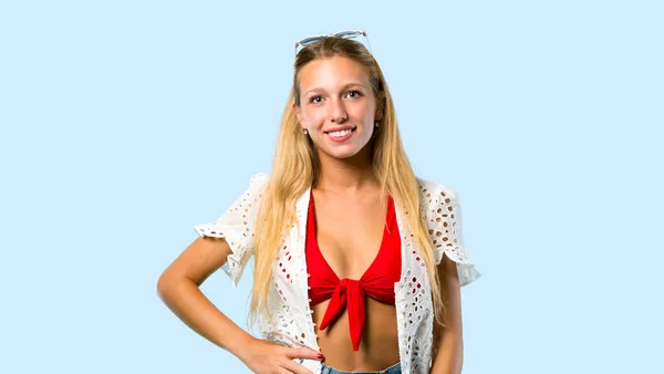 金发女孩在暑假摆姿势与手臂在臀部和微笑的蓝色背景 — 图库照片