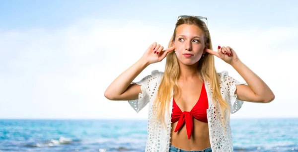 Chica rubia en vacaciones de verano cubriendo las orejas con las manos en el b — Foto de Stock
