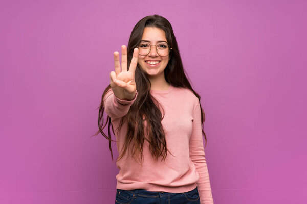 Teenager girl over purple wall happy and counting three with fingers