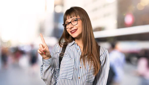 Woman with glasses showing and lifting a finger in sign of the best at outdoors