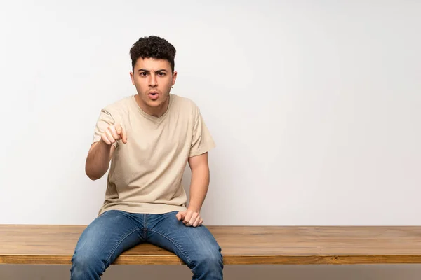 Young Man Sitting Table Surprised Pointing Front — 스톡 사진